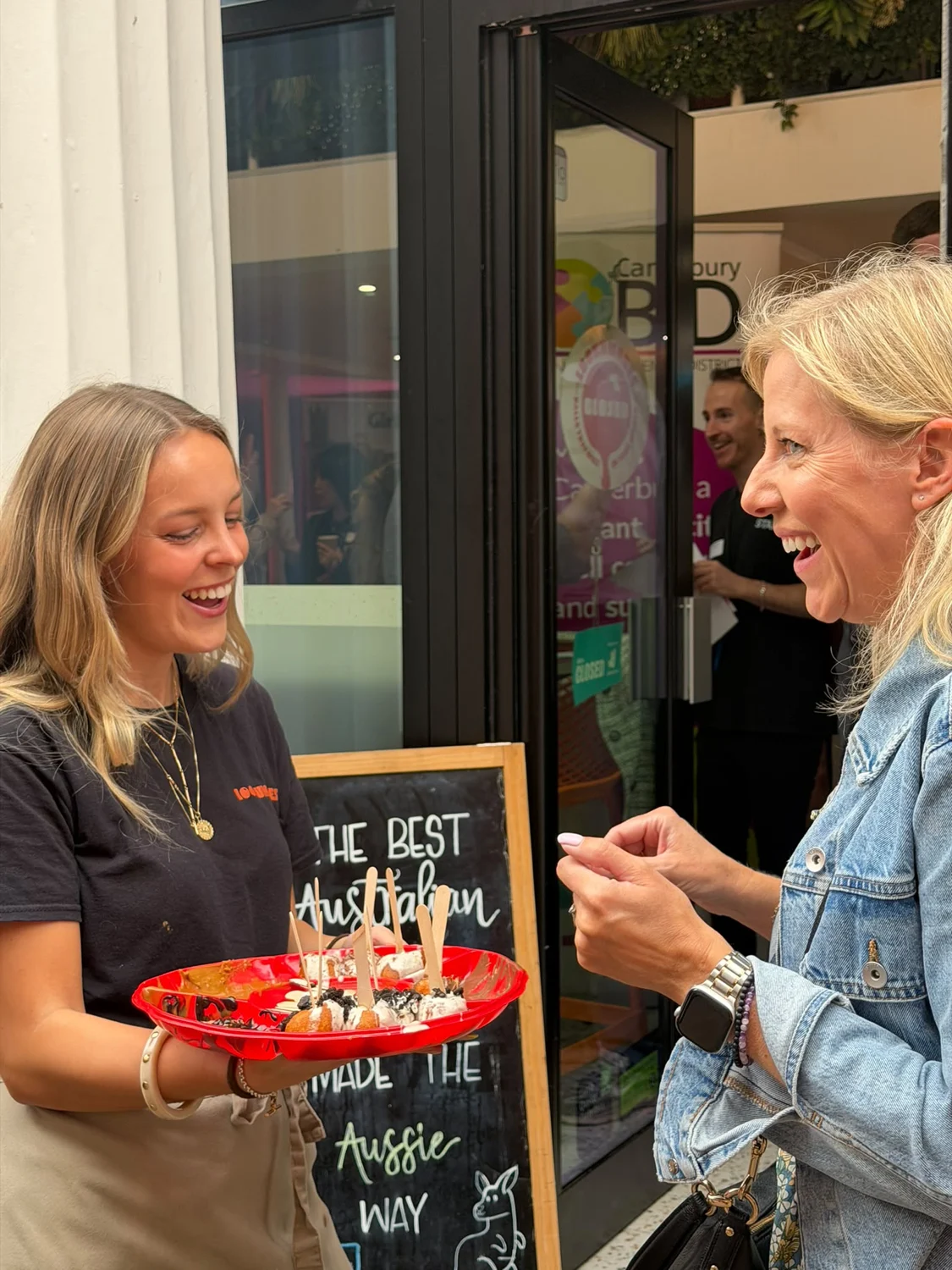A Lookumades team member offering Loukoumades to a guest outside the shop